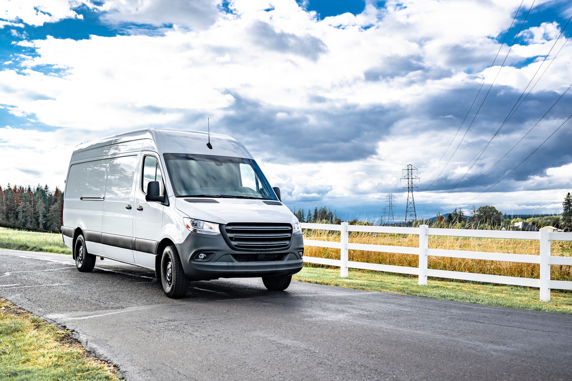 Compact cargo white mini van for small business and local deliveries running on the narrow road with meadows on the sides